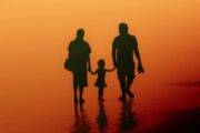 Silloutte of Mother, toddler and father walking away from camera with yellow/orange background like sunset