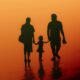 Silloutte of Mother, toddler and father walking away from camera with yellow/orange background like sunset