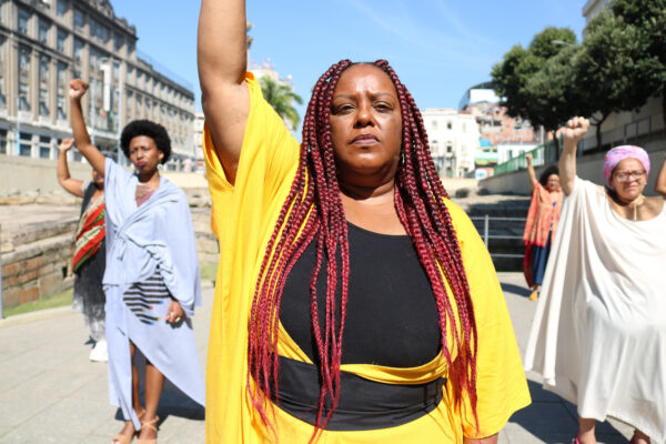 Monica Francisco holds her fist up in the middle of a streat, surrounded by other Black Brazilian women.