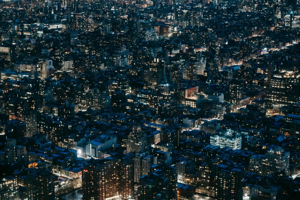 Cityscape shot from above at night, with dense buildings, lights are on in some but not all windows.